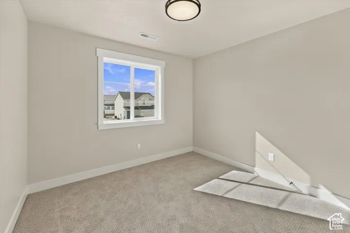 Neutral-toned interior featuring wall-to-wall carpeting, window with craftsman-style trim, and a flush-mount overhead light fixture