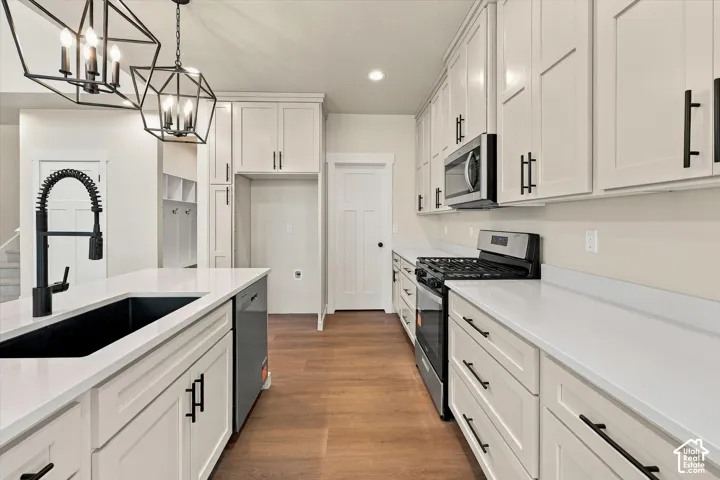 Kitchen featuring white shaker-style cabinetry, quartz countertops, a matte black faucet with a pull-down sprayer, wood-finish flooring, and geometric pendant lighting