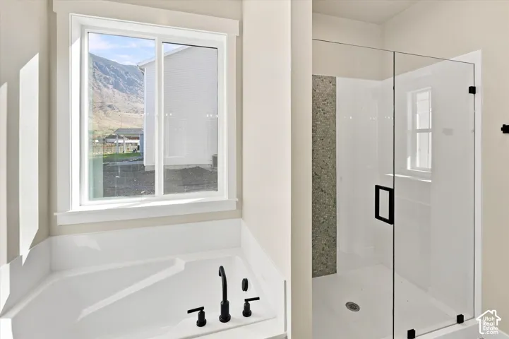 Soaking tub with a matte black faucet, glass-enclosed shower with a decorative stone-finish tile inlay, and large-format window framing mountain scenery