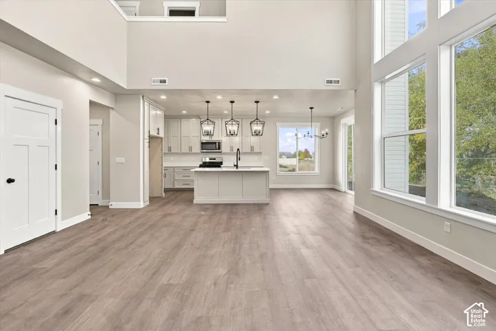 Open-concept interior featuring double-height ceilings, wood-finish flooring, floor-to-ceiling windows, custom cabinetry, and a central kitchen island with pendant lighting