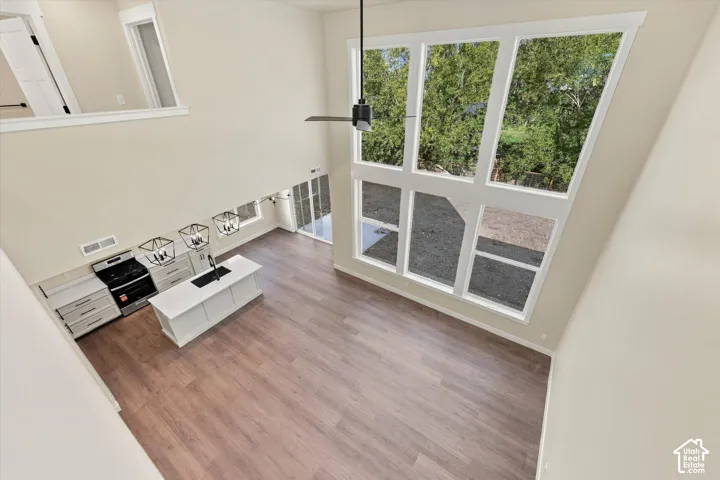 Double-height ceiling with expansive multi-pane windows, wood-finish flooring, kitchen island with built-in sink, and pendant lighting