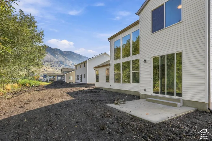 Exterior elevation featuring light-colored horizontal siding, expansive multi-pane windows, sliding glass door, concrete patio, and mountain backdrop