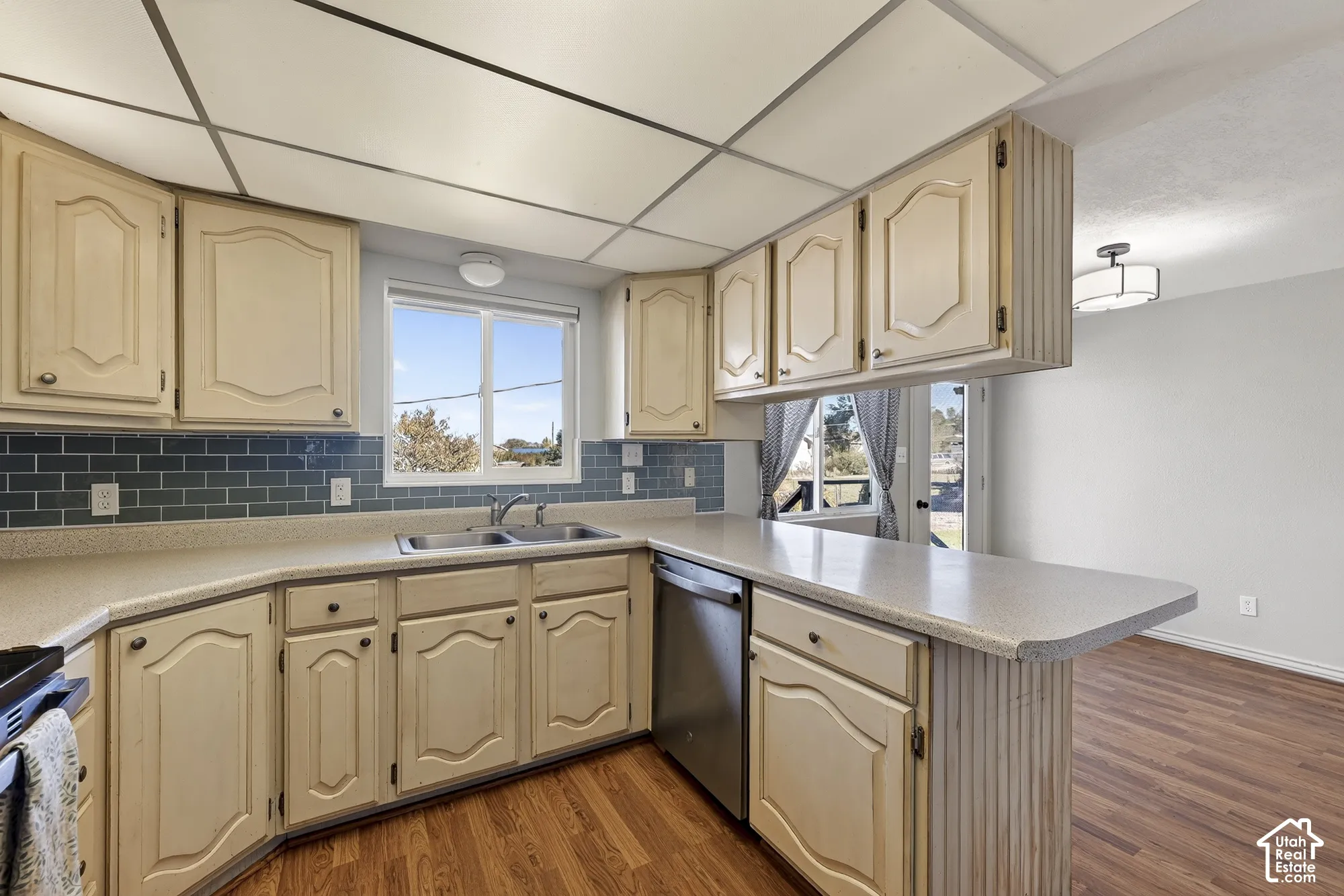 Kitchen featuring wood-finish cabinetry, a blue subway tile backsplash, solid-surface countertops, a stainless steel dishwasher, and wood-finish flooring