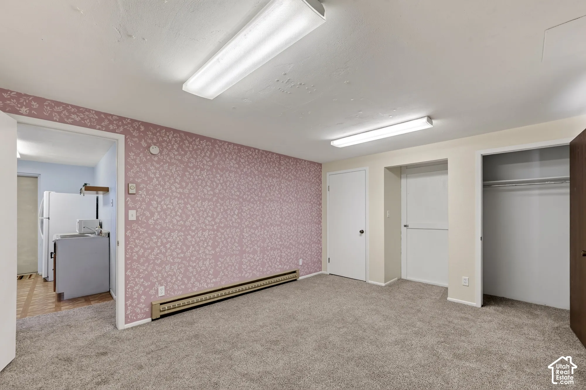 Room featuring patterned wallpaper, neutral carpeting, double linear overhead lighting, and built-in closet storage