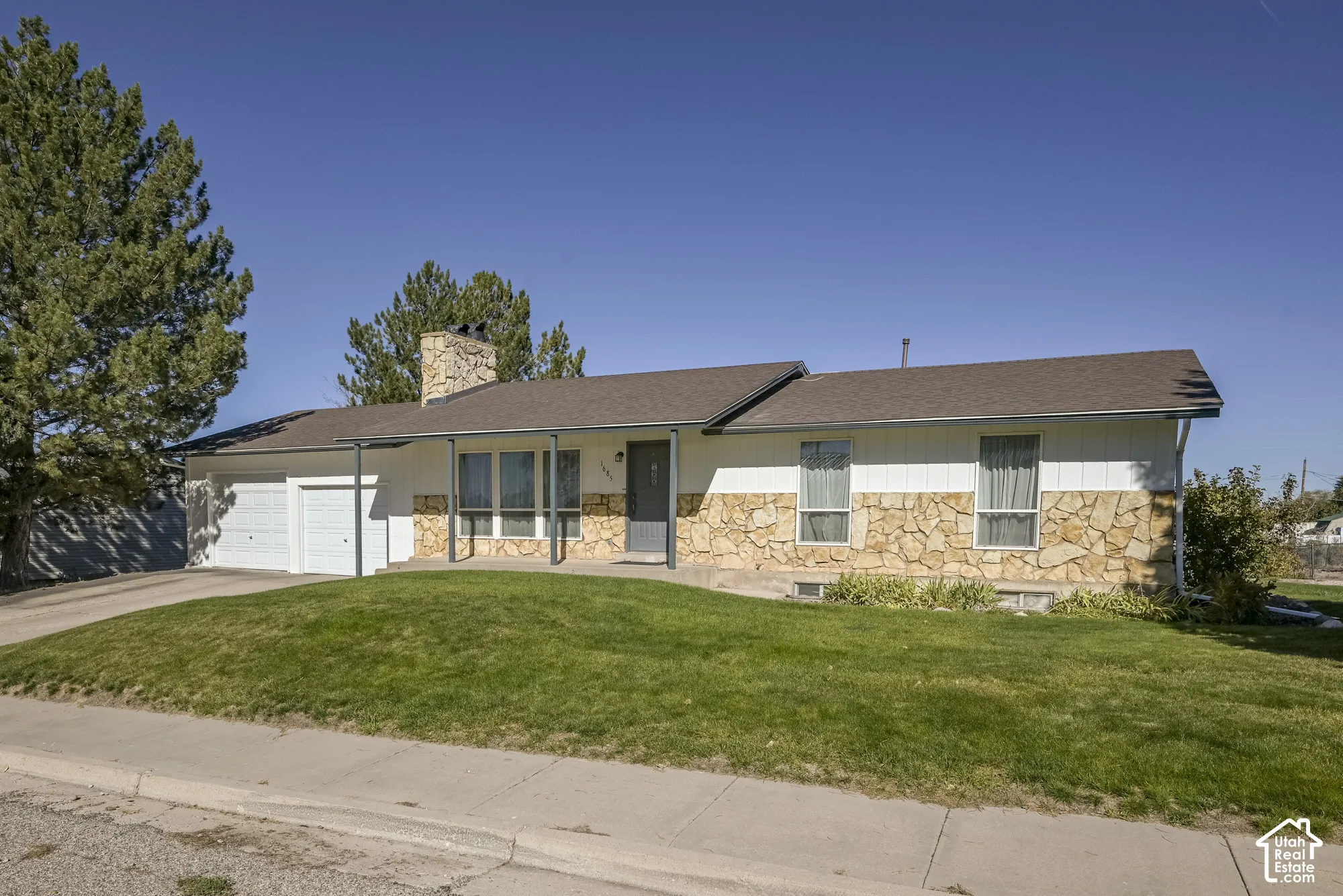 Single-level exterior featuring a stone masonry facade, horizontal siding, attached two-car garage, and a chimney
