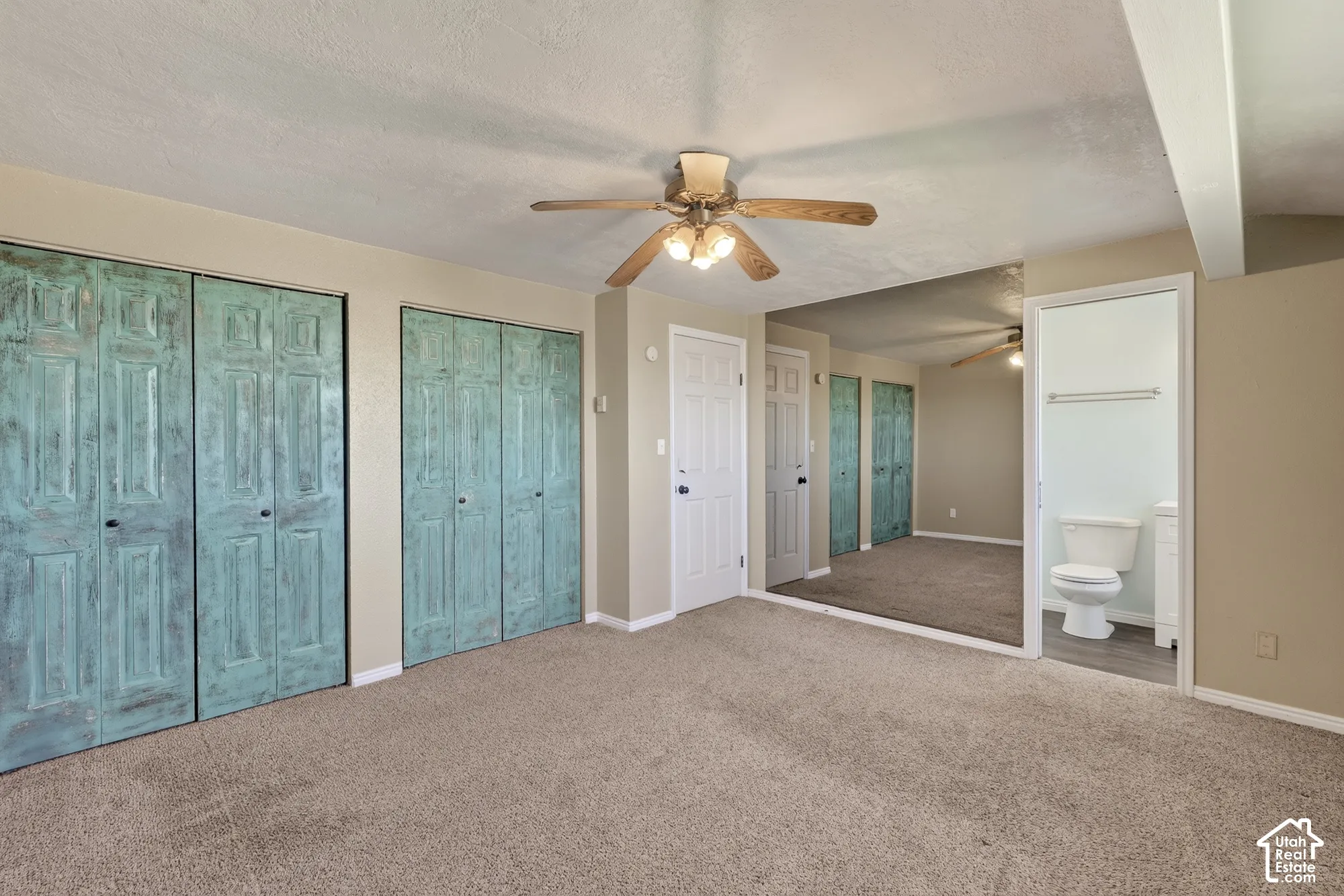 Room featuring carpeting, dual sets of bi-fold closet doors with a distressed finish, a ceiling fan with integrated lighting, and a mirrored wall surface