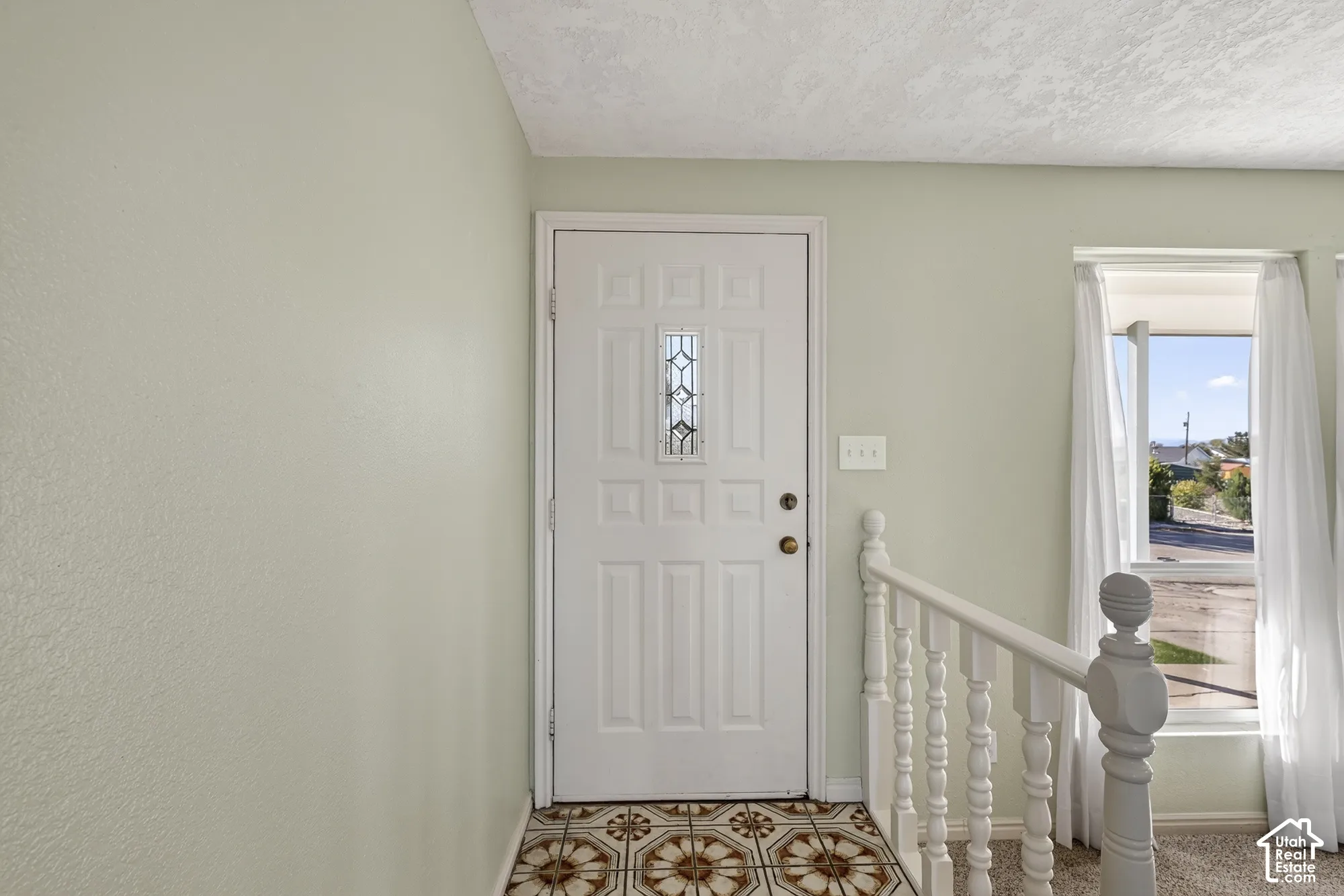 Entry featuring a white six-panel door with decorative glass insert, patterned tile flooring, and painted white balustrade railing