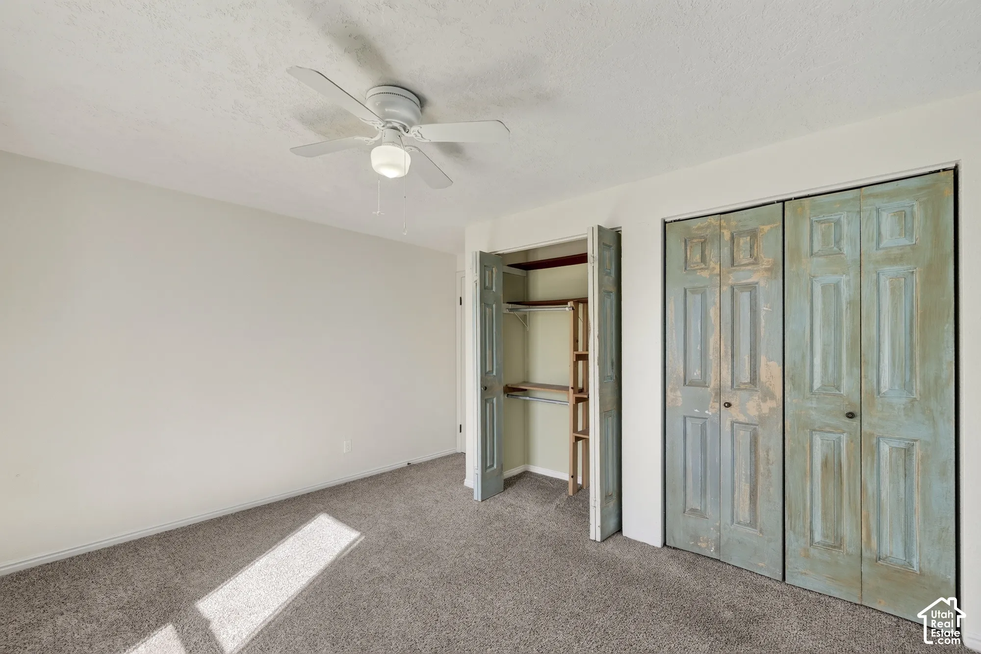 Room featuring neutral carpeting, a ceiling fan with integrated lighting, and dual bi-fold closet doors with a distressed finish