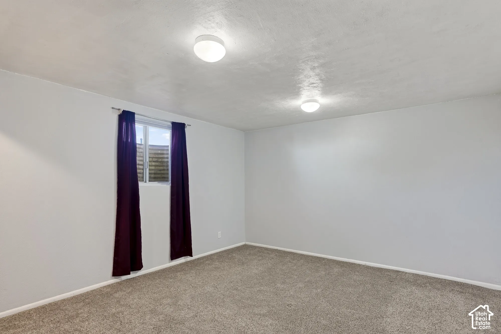 Neutral-toned wall finish, wall-to-wall carpeting, dual ceiling-mounted light fixtures, and a single-pane window