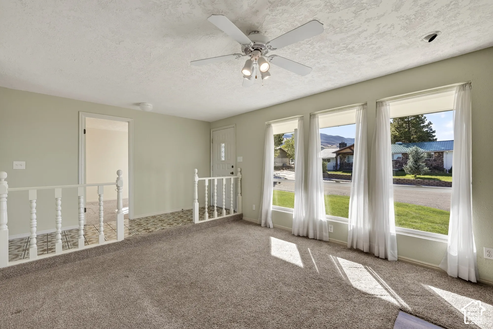 Living space featuring a central ceiling fan with integrated lighting, oversized picture windows, and a classic balustrade railing bordering a tiled landing area