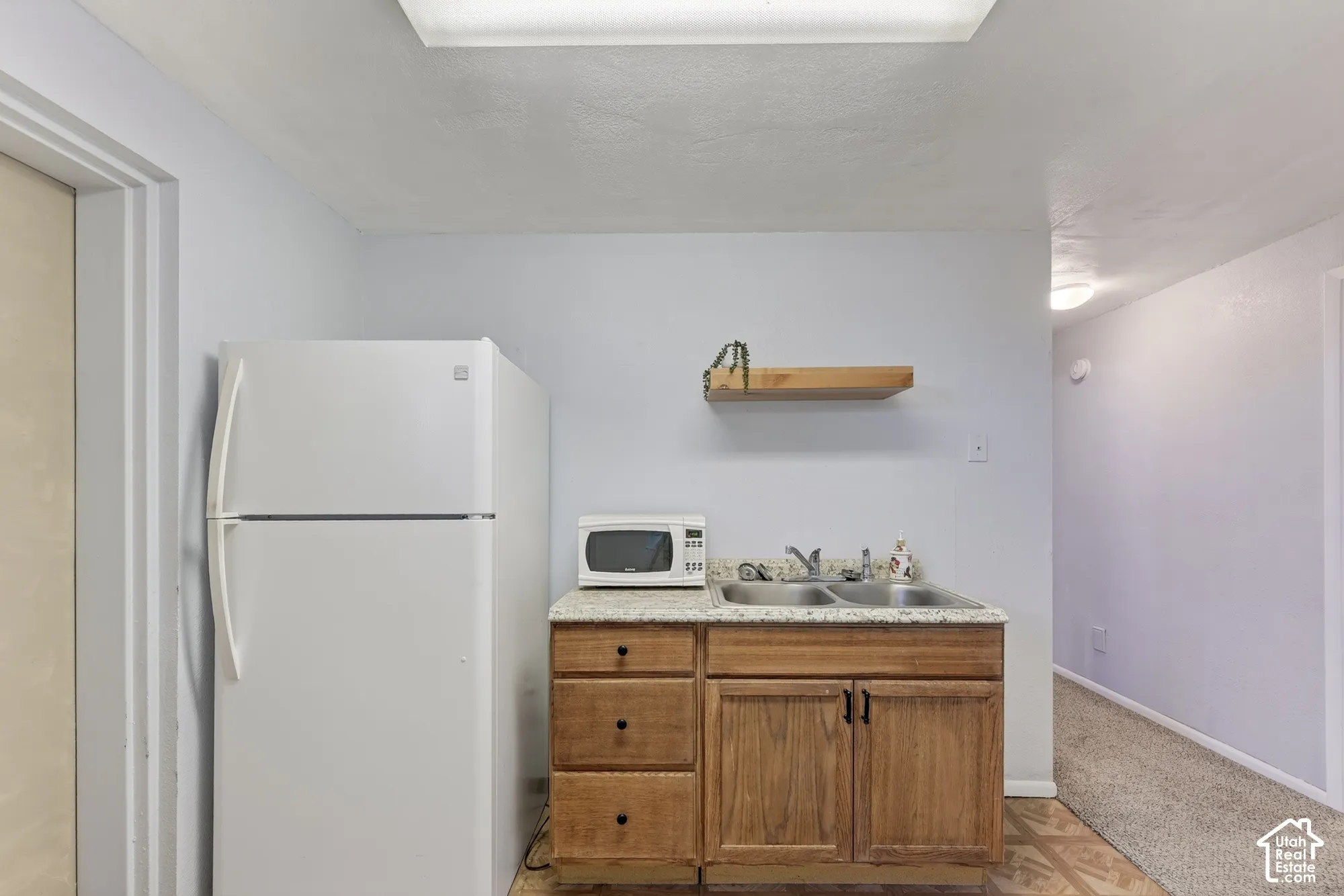 Wet bar area featuring wood cabinetry, stone-finish countertop, dual-basin sink, and wall-mounted floating wood shelf