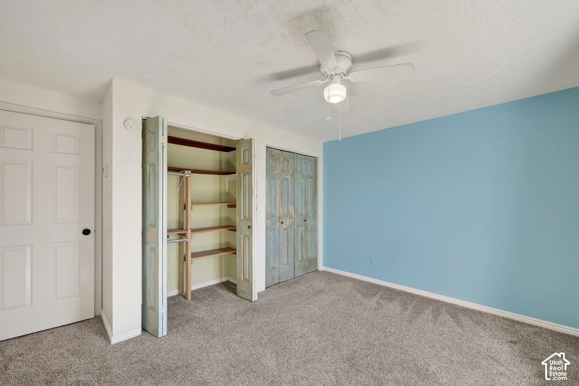 Room featuring neutral carpeting, dual closets with built-in shelving, and a ceiling-mounted light fixture with a fan
