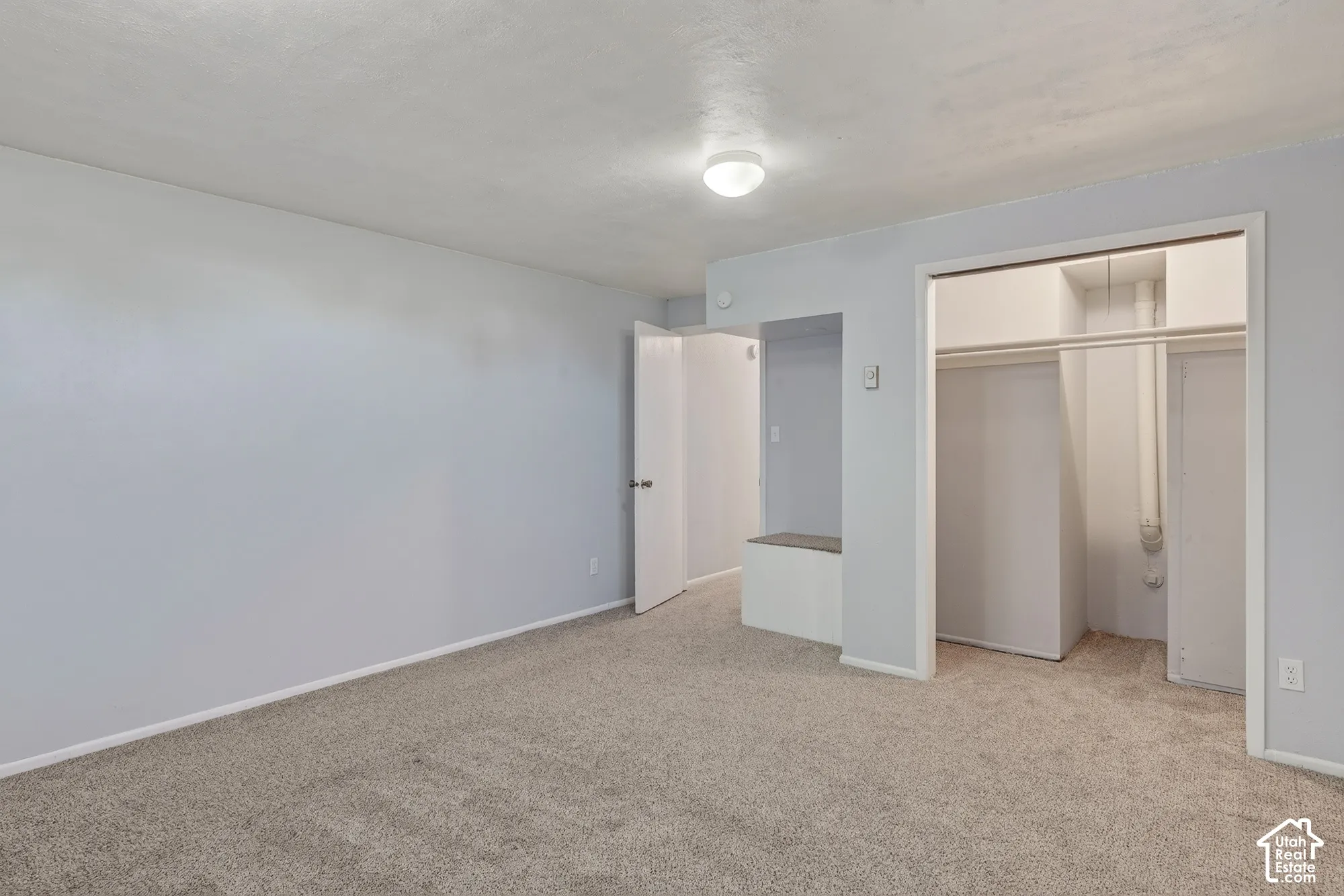 Interior space featuring neutral-toned carpeting, smooth-finish walls, a flush-mount ceiling light fixture, a built-in storage bench, and a walk-in closet with overhead shelving