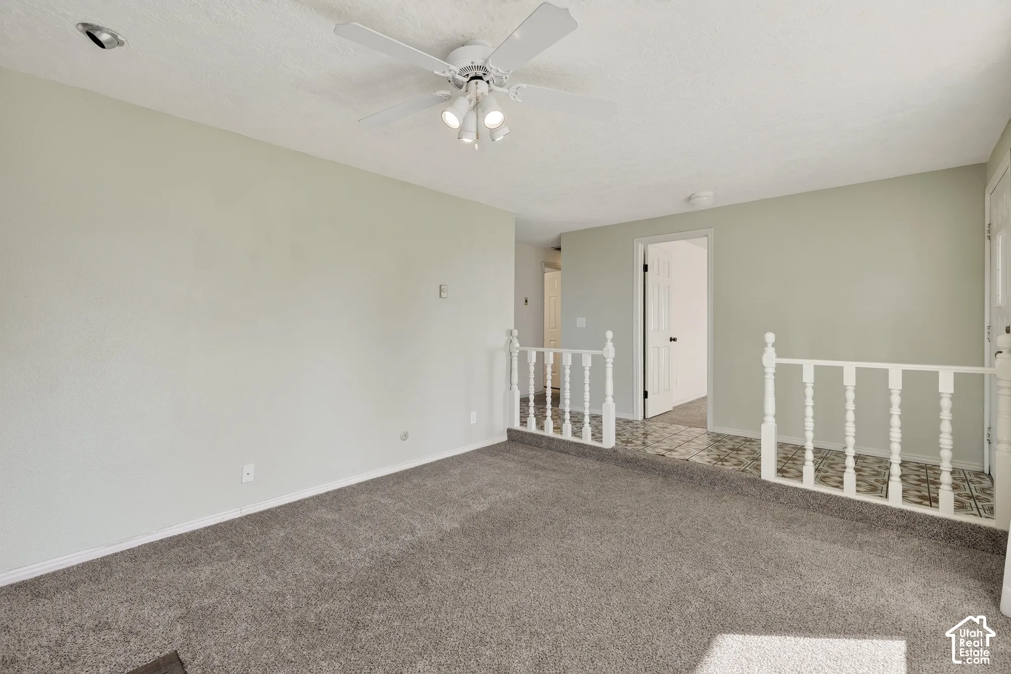 Spacious interior featuring wall-to-wall carpeting, a ceiling-mounted light fixture with a fan, and a decorative white spindle railing