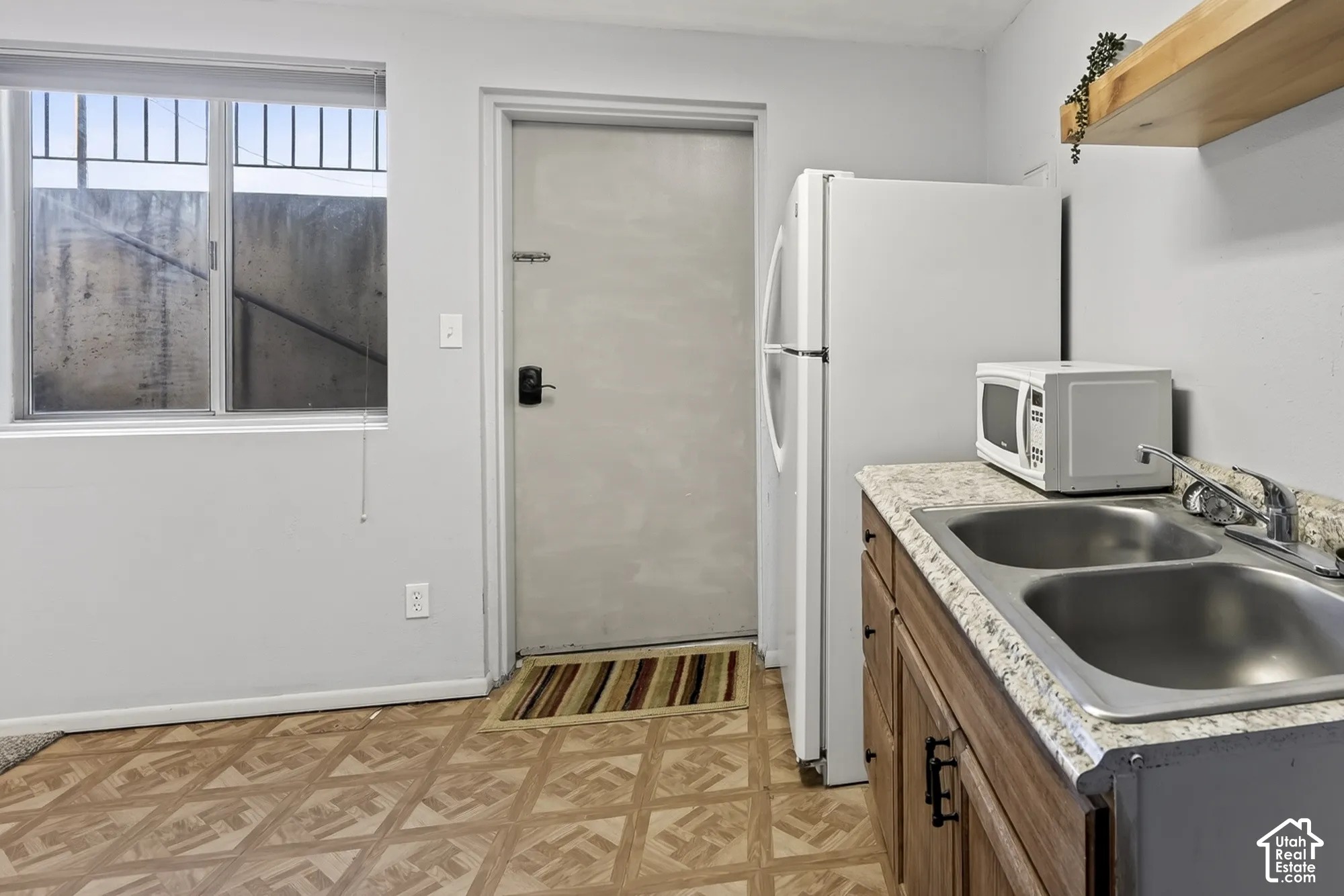Kitchen area featuring wood-finish cabinetry, stone-patterned laminate countertops, dual-basin stainless steel sink, and floating wall-mounted shelving