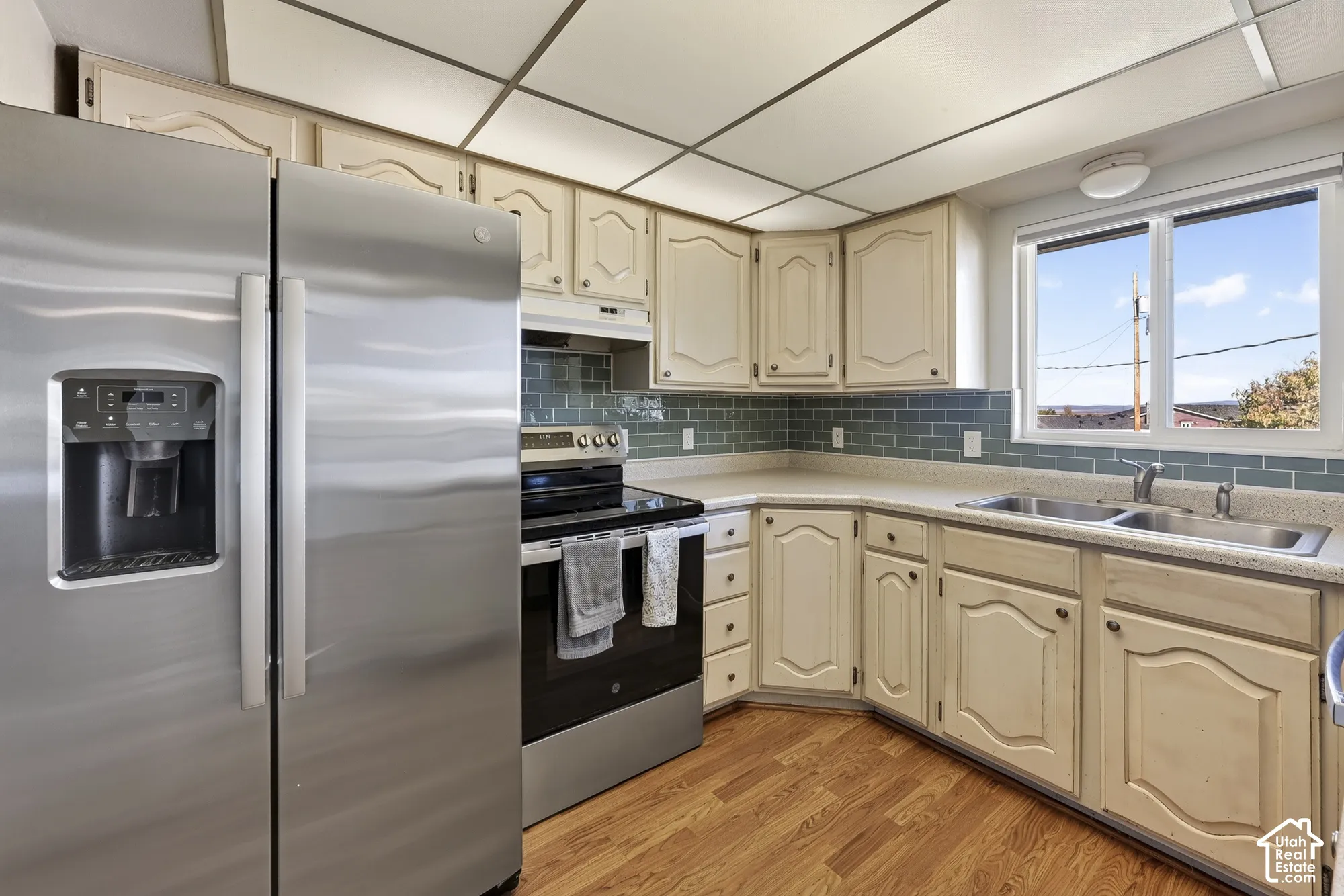 Kitchen featuring stainless steel appliances, wood-finish cabinetry, subway tile backsplash, laminate countertops, and wood-finish flooring