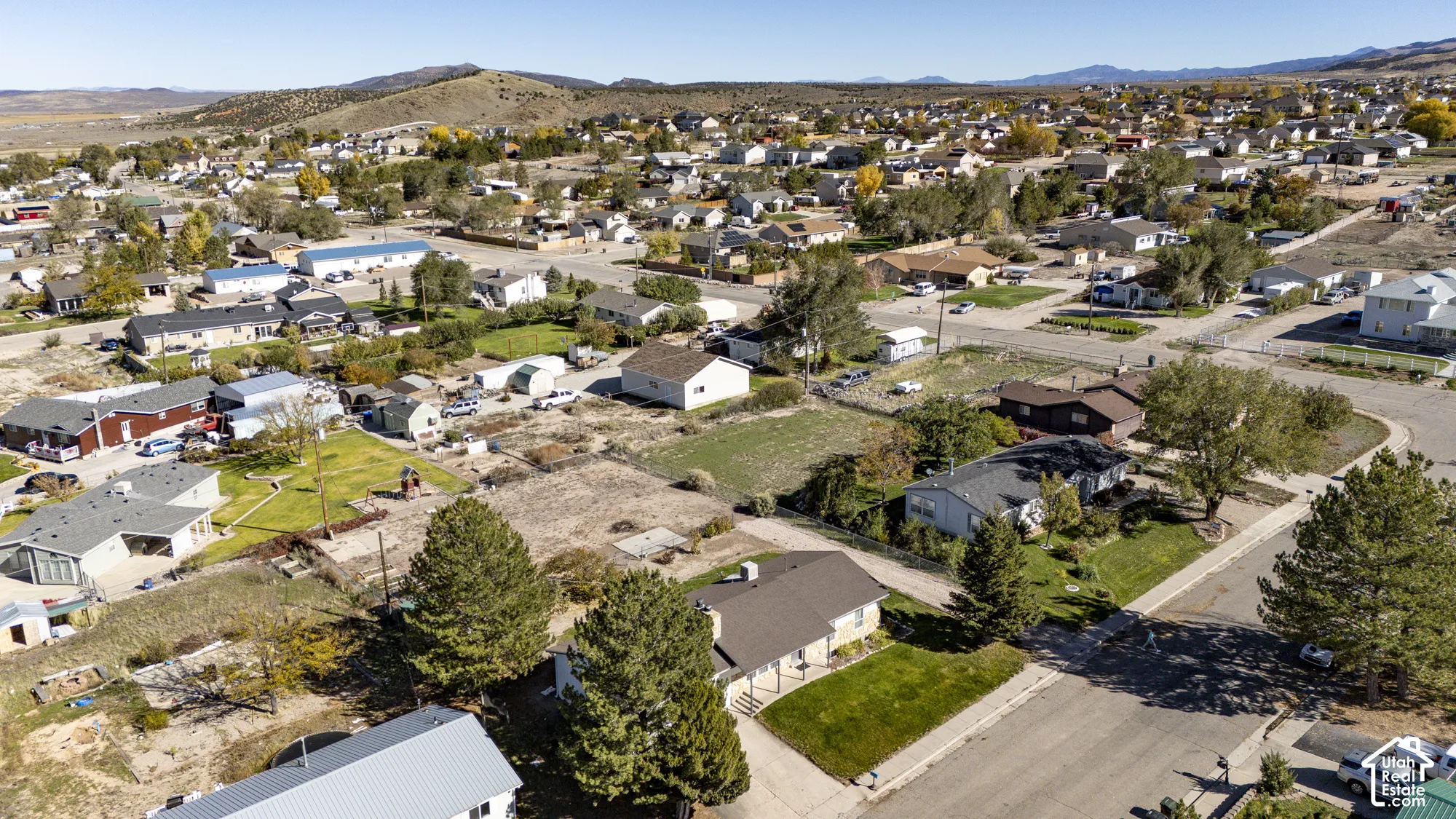 Aerial perspective of the property featuring a paved street, established landscaping, mature pine trees, and a mountain backdrop