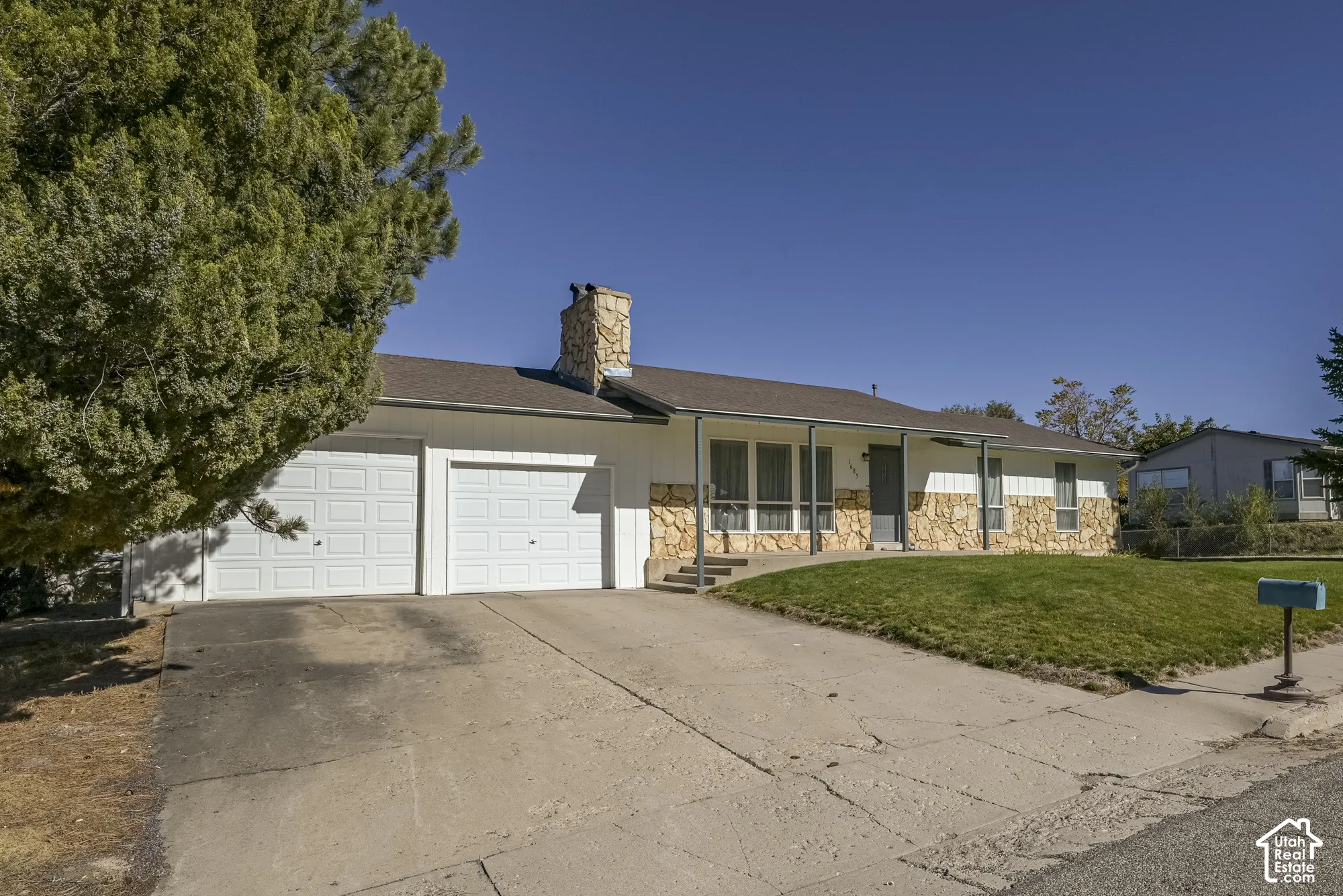 Exterior featuring white siding, stone veneer accents, a stone chimney, a covered porch, and a two-car garage