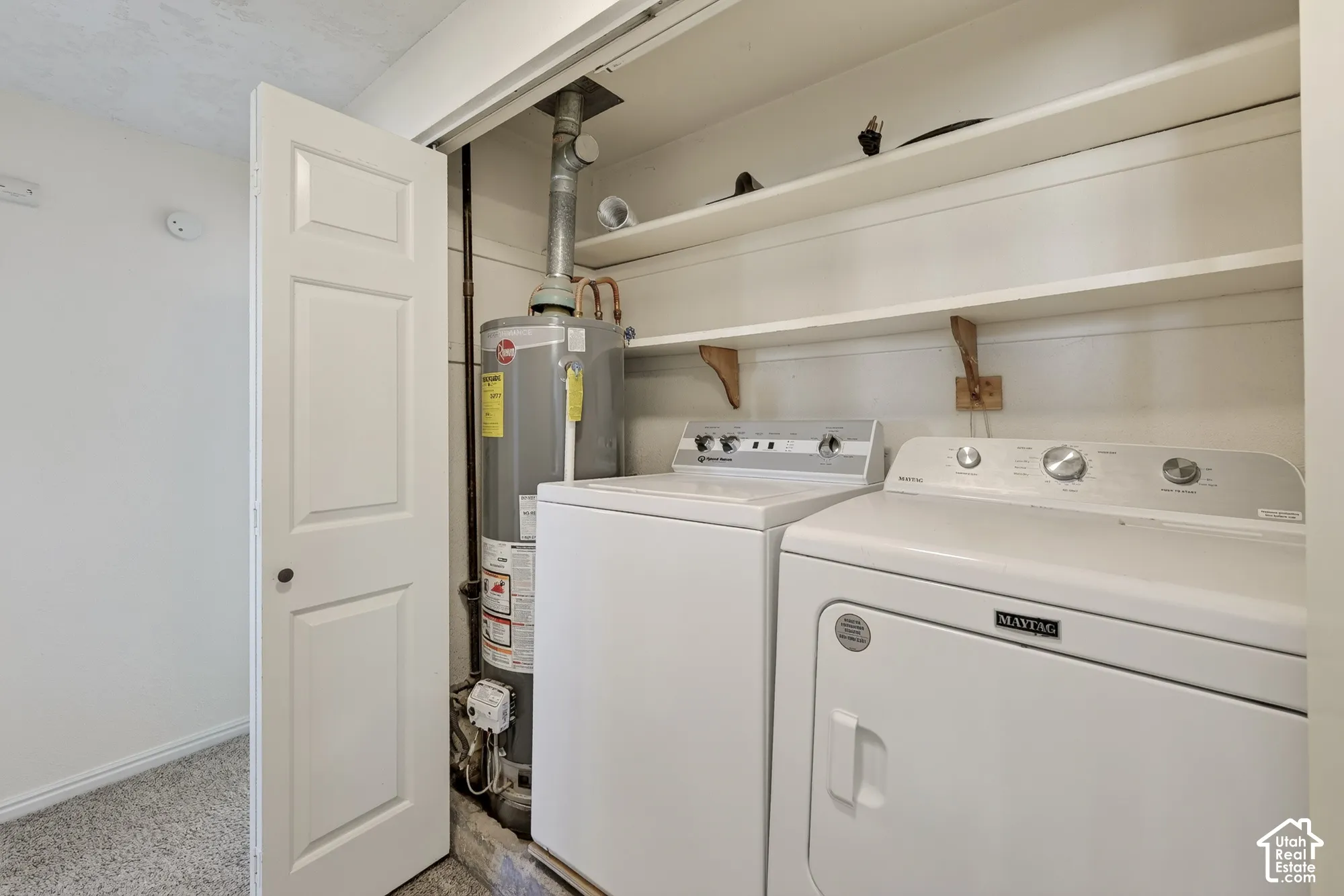 Dedicated utility closet featuring a white-finish clothes washer and dryer, a vertical water heater, and two built-in storage shelves