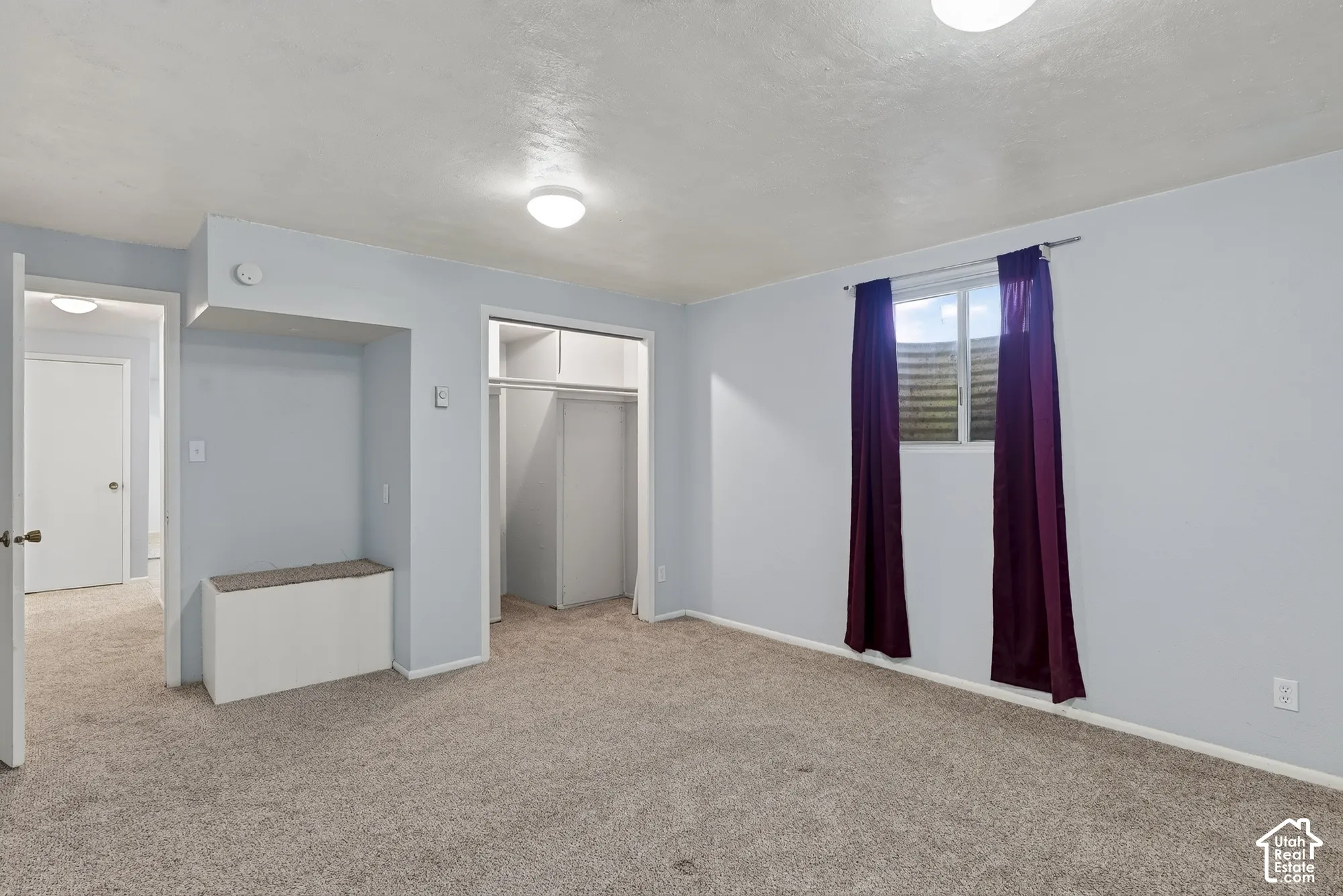 Room featuring neutral-toned carpeting, a built-in bench, a dedicated closet with sliding doors, and a window with a window well