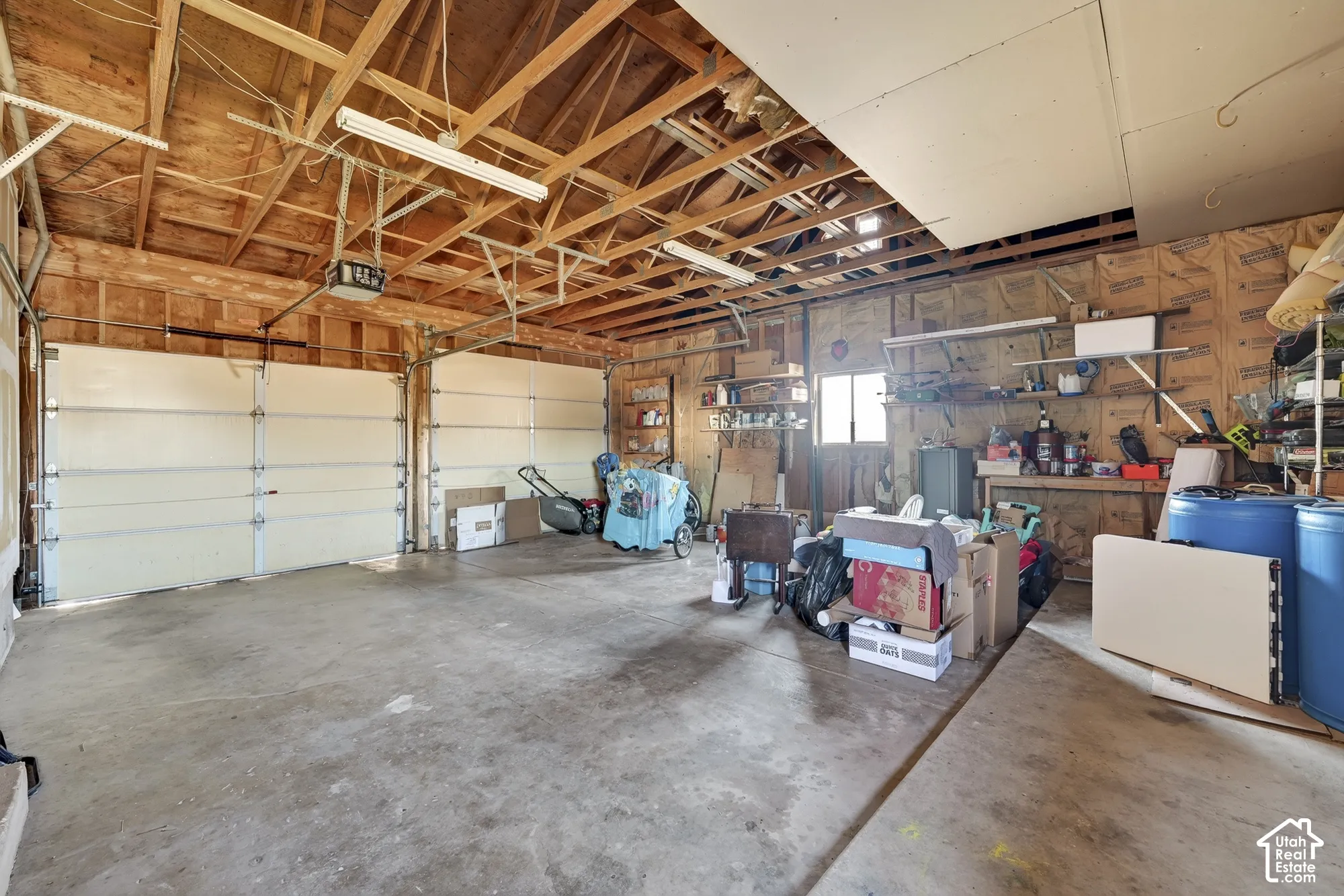 Two-car garage featuring exposed wood framing, concrete flooring, dual overhead garage doors, and integrated fluorescent lighting