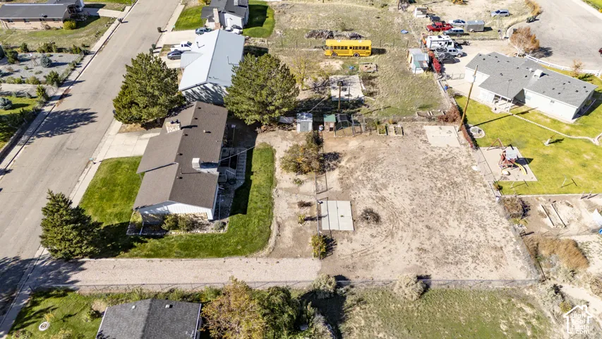 Aerial perspective of a multi-level residence featuring a pitched shingle roof, chimney, attached paved driveway, and expansive lot with perimeter fencing