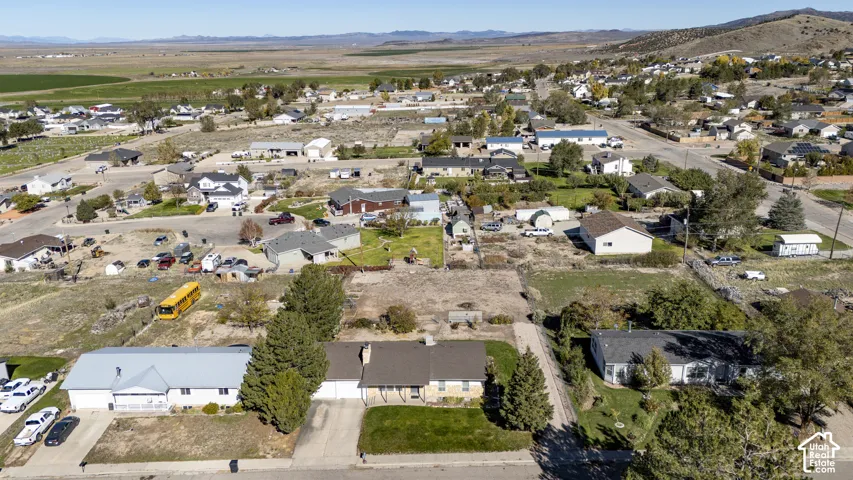 Aerial view of a residential property featuring a single-story home with a multi-gabled roofline, stone and siding exterior, attached garage, and surrounding mature trees