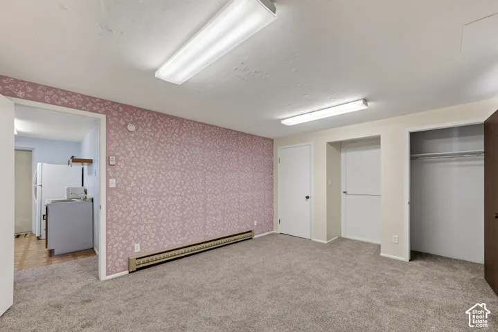 Room featuring patterned wallpaper, neutral carpeting, double linear overhead lighting, and built-in closet storage