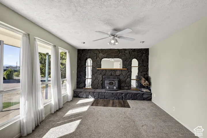 Floor-to-ceiling rock fireplace with a built-in hearth, integrated display niches, large picture windows, and a ceiling fan