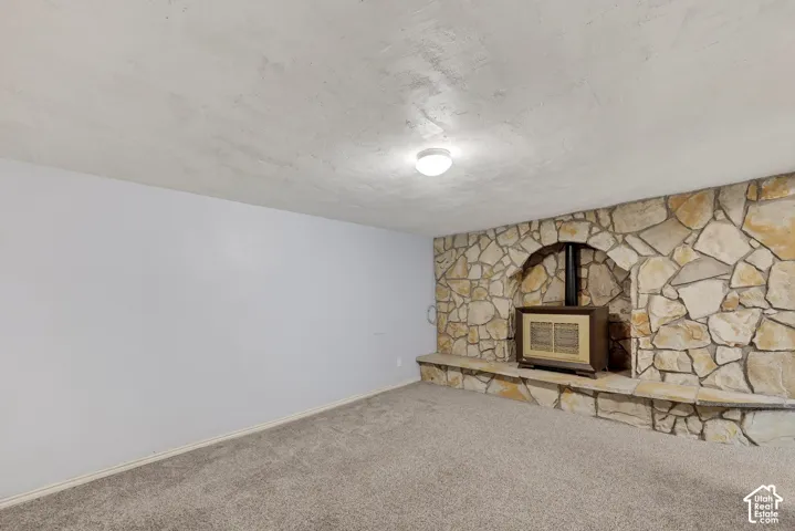 Full-height stone wall with an integrated arched hearth, built-in stone bench, metal stove insert, and neutral carpeting