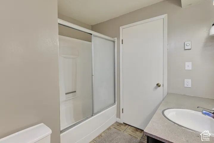 Bathroom featuring a shower and bathtub combination with sliding glass doors, a vanity with a stone-finish countertop, an integrated oval sink, and a white interior door