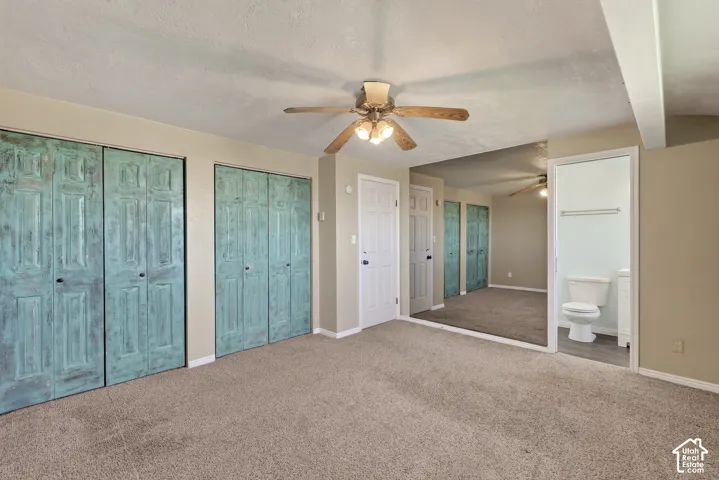 Room featuring carpeting, dual sets of bi-fold closet doors with a distressed finish, a ceiling fan with integrated lighting, and a mirrored wall surface