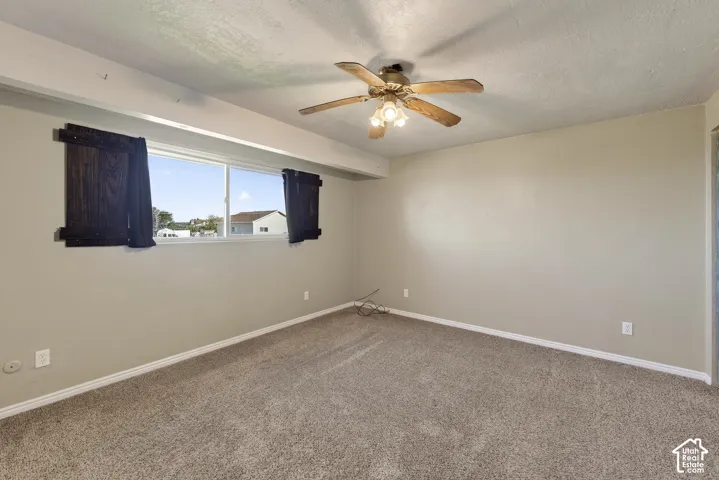 Room featuring neutral wall tones, wall-to-wall carpeting, a large sliding window, and a ceiling fan with integrated lighting