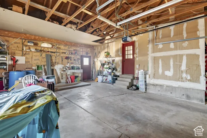 Garage space featuring an exposed wood-beam ceiling, concrete flooring, built-in wall shelving, and two exterior access doors with multi-pane glass detailing