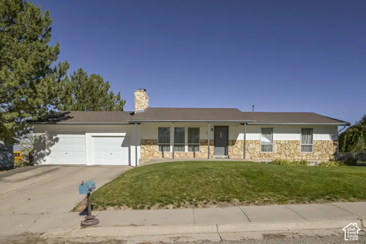 Single-story exterior featuring white vertical siding, natural stone accents, a stone chimney, a covered porch, and a two-car garage