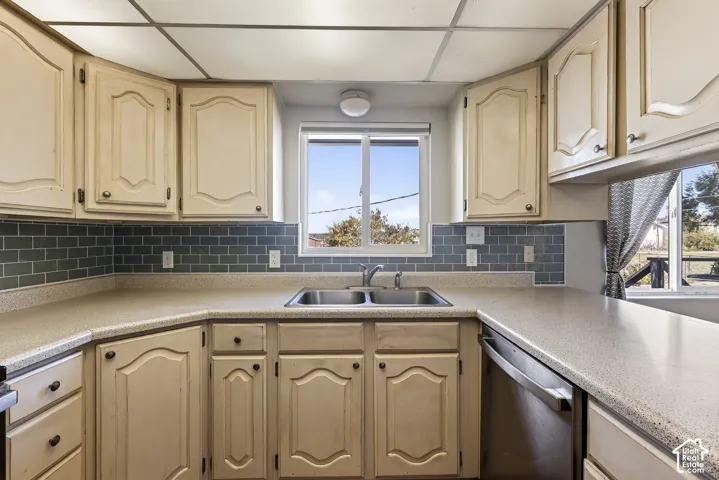 Kitchen featuring raised-panel cabinetry, solid-surface countertops, blue subway tile backsplash, stainless steel dual-basin sink, and a drop-in dishwasher