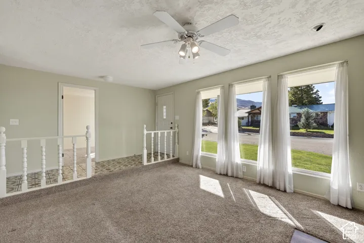 Living space featuring a central ceiling fan with integrated lighting, oversized picture windows, and a classic balustrade railing bordering a tiled landing area