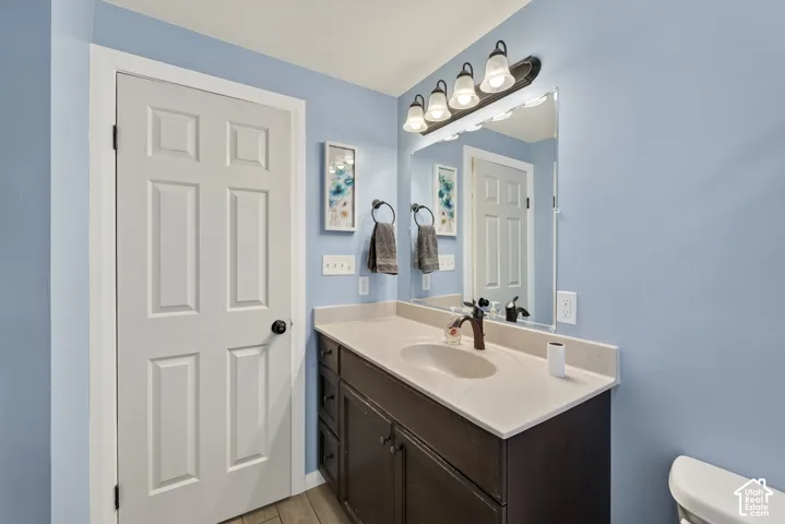 Bathroom vanity featuring a dark-finish wood cabinet, light solid-surface countertop with an integrated basin, wall-mounted four-light fixture, and a large frameless mirror
