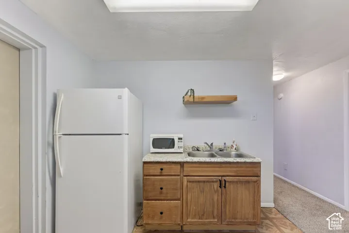 Wet bar area featuring wood cabinetry, stone-finish countertop, dual-basin sink, and wall-mounted floating wood shelf