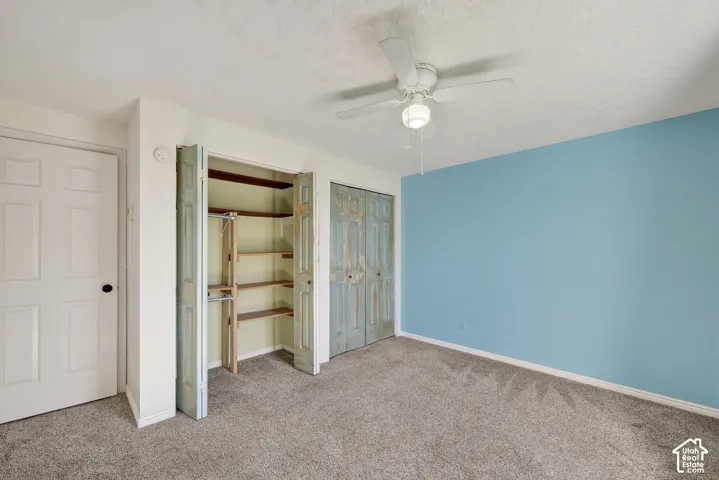 Room featuring neutral carpeting, dual closets with built-in shelving, and a ceiling-mounted light fixture with a fan