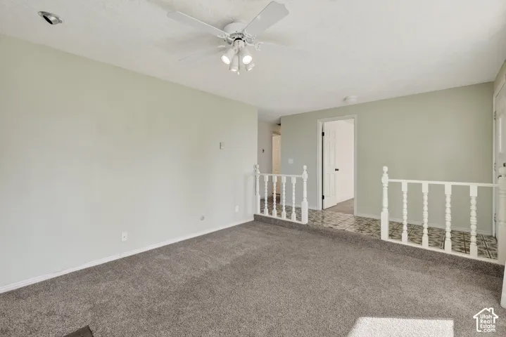 Spacious interior featuring wall-to-wall carpeting, a ceiling-mounted light fixture with a fan, and a decorative white spindle railing