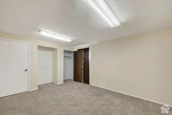 Neutral-toned interior space featuring neutral wall-to-wall carpeting, two ceiling-mounted rectangular light fixtures, and two interior doors providing access to closet storage