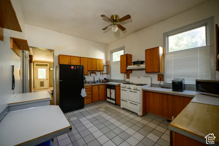 Kitchen featuring wood cabinetry, tiled flooring, built-in range, dual windows, and ceiling fan