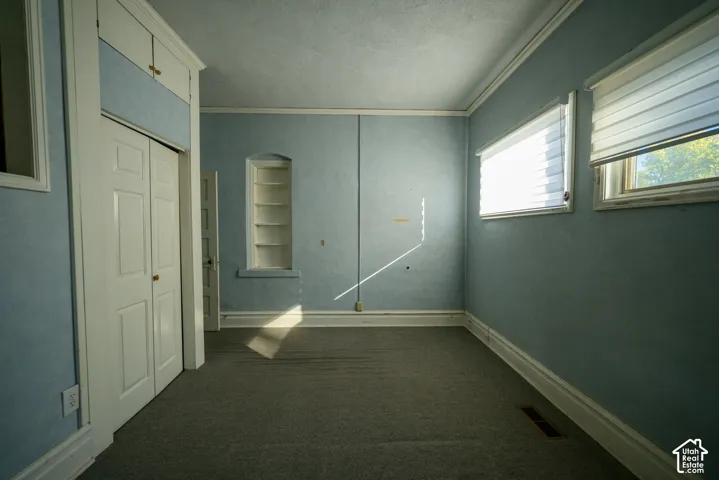 Interior room featuring built-in cabinetry, recessed wall shelving, multi-panel doors, crown molding, and dual windows with fitted shades