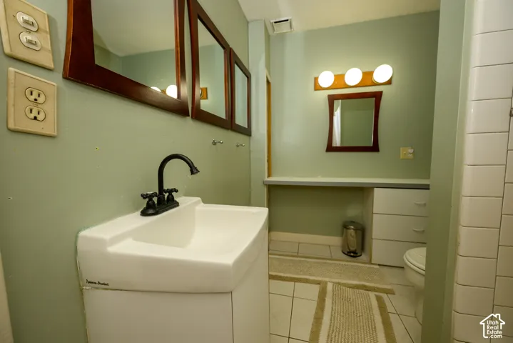 Bathroom vanity with a white basin and matte black gooseneck faucet, built-in white cabinetry, three-light vanity fixture, and tiled flooring