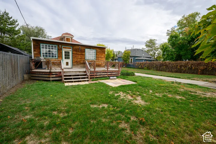 Wood-sided exterior featuring a raised wooden deck with railings, multi-pane windows, and an expansive lawn