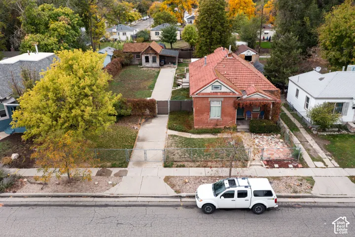 Brick exterior residence featuring a tiled gable roof, concrete driveway, fenced yard, and mature landscape