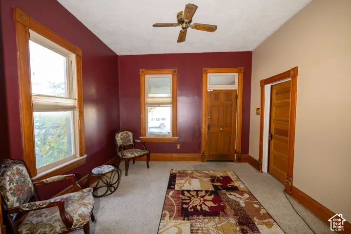 Interior space featuring natural wood-finish window and door trim, multi-panel wood door with transom, and ceiling fan