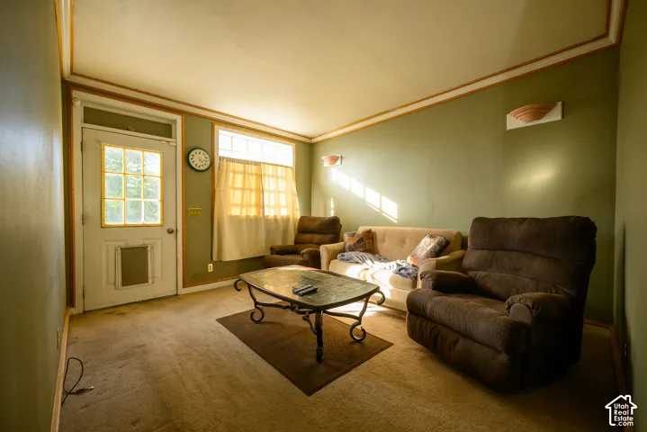 Living space featuring crown molding, wall-mounted sconce lighting, and a multi-pane exterior door with a transom window