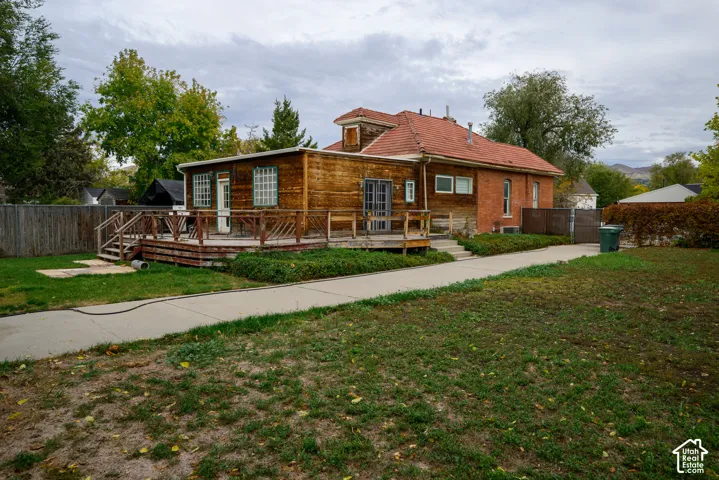 Exterior featuring a red clay tile roof, brick masonry siding, wood-plank siding, and a wooden deck with stairs